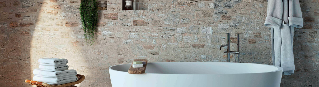Ein stilvolles Bad mit freistehender Wanne, Ziegelwand, Handtuchhocker, Bademantel und Wandnischen mit Pflanzen und Pflegeprodukten. Ein stilvolles Bad mit freistehender Wanne, Ziegelwand, Handtuchhocker, Bademantel und Wandnischen mit Pflanzen und Pflegeprodukten.