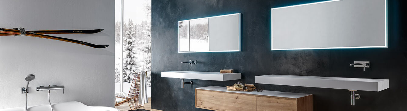 Badezimmer mit freistehender Badewanne, beleuchteten Spiegeln, Holzwaschtisch, Skiern an der Wand und großem Fenster. Elegante, gemütliche Atmosphäre. Badezimmer mit freistehender Badewanne, beleuchteten Spiegeln, Holzwaschtisch, Skiern an der Wand und großem Fenster. Elegante, gemütliche Atmosphäre.