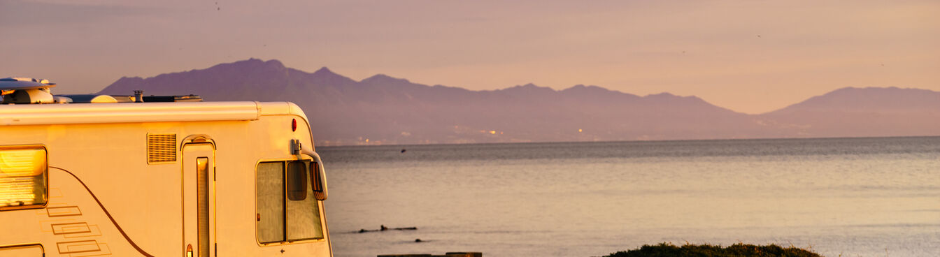 Ein Wohnmobil steht in einer malerischen Küstenlandschaft bei Sonnenuntergang. Im Hintergrund sind das Meer und Berge zu sehen, während der Himmel in warmen Farben leuchtet. Ein Wohnmobil steht in einer malerischen Küstenlandschaft bei Sonnenuntergang. Im Hintergrund sind das Meer und Berge zu sehen, während der Himmel in warmen Farben leuchtet.