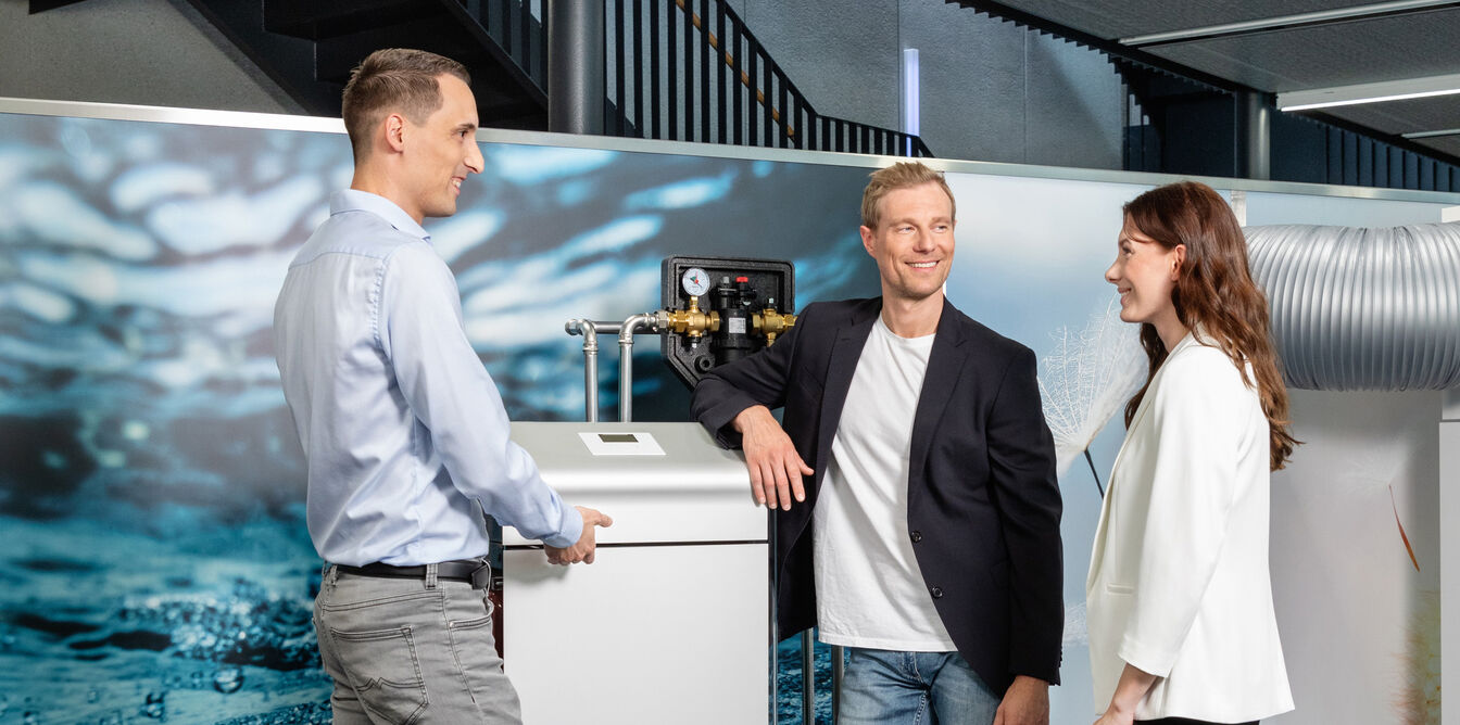Eine Gruppe von drei Personen steht lächelnd um ein technisches Gerät in einem modernen Energiepark, vor einem Hintergrund mit Wasserbild. Eine Gruppe von drei Personen steht lächelnd um ein technisches Gerät in einem modernen Energiepark, vor einem Hintergrund mit Wasserbild.