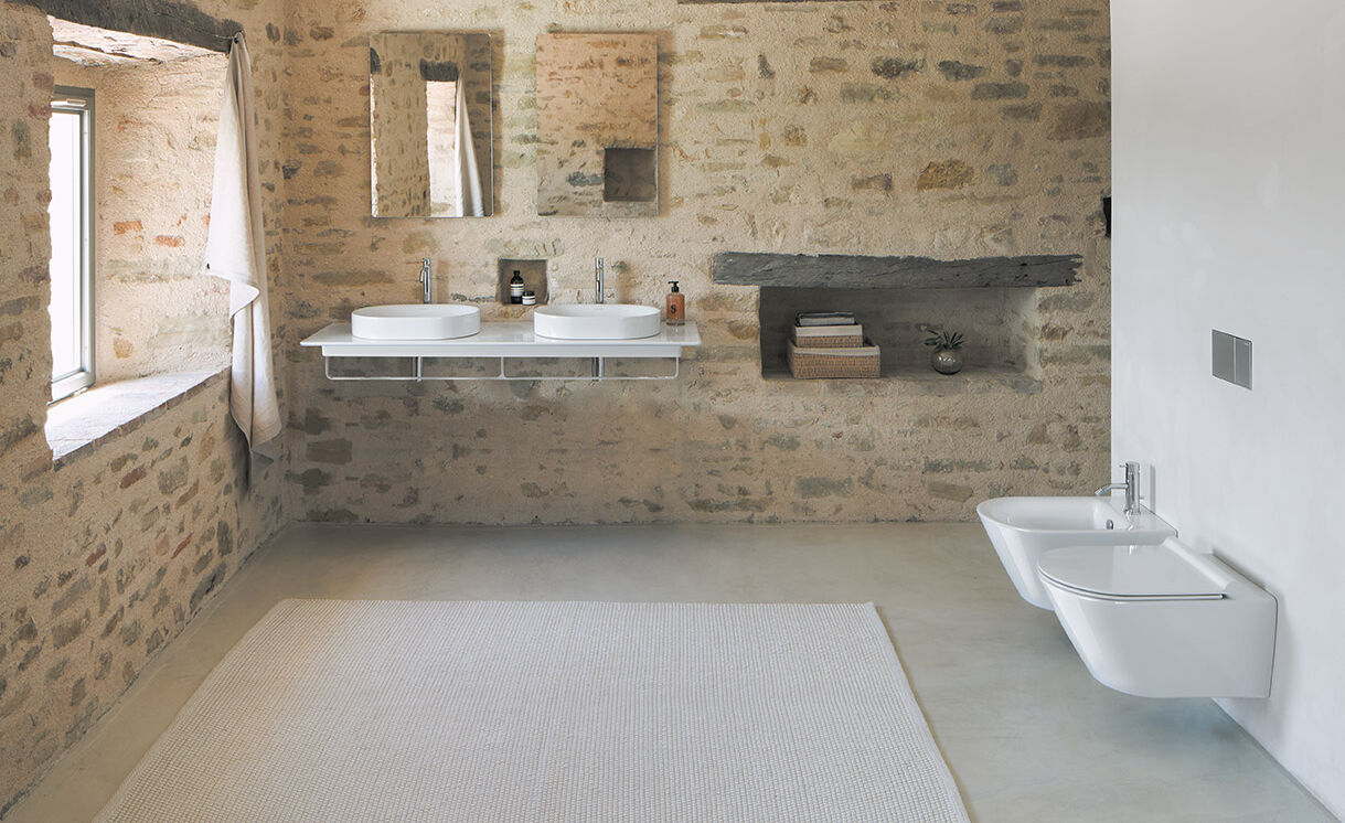 Rustikales Badezimmer mit Steinwänden, Doppelwaschbecken, modernen WC und Bidet. Integrierte Ablage, helle Fensterbeleuchtung, schwebende Ablage. Rustikales Badezimmer mit Steinwänden, Doppelwaschbecken, modernen WC und Bidet. Integrierte Ablage, helle Fensterbeleuchtung, schwebende Ablage.