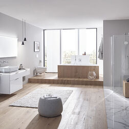 Inhaus Smaragd Optima X Geräumiges, modernes Badezimmer mit freistehender Badewanne, Glasdusche, Waschtisch und Spiegel. Heller Holzboden, graue Wände und große Fenster.