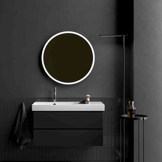 Ein elegantes, minimalistisches Badezimmer mit schwarzem Waschtisch, rundem beleuchteten Spiegel und dunklen W&auml;nden, erg&auml;nzt durch einen schlanken Beistelltisch.