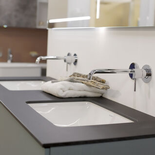 Moderner Waschtisch mit zwei integrierten Waschbecken, eleganten Wandarmaturen und gefalteten Handtüchern auf dunkler Oberfläche. Moderner Waschtisch mit zwei integrierten Waschbecken, eleganten Wandarmaturen und gefalteten Handtüchern auf dunkler Oberfläche.