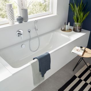 Modernes Badezimmer mit eingebauter Wanne, blauer Akzentwand, Pflanzen, gestreiftem Teppich und stilvollen Dekorationen f&uuml;r gem&uuml;tliches Ambiente.