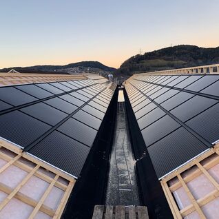 Solarpaneele auf einem V-förmigen Dach, eingebettet in eine hügelige Landschaft bei Sonnenuntergang. Solarpaneele auf einem V-förmigen Dach, eingebettet in eine hügelige Landschaft bei Sonnenuntergang.