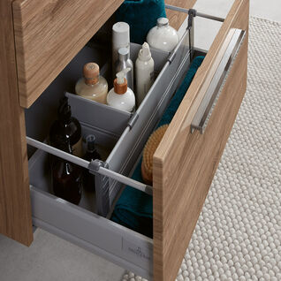 Nahaufnahme eines Holzschranks im Bad. Schublade organisiert mit Pflegeprodukten und Handtüchern. Moderne Griffe und strukturierter Teppich ergänzen das Design. Nahaufnahme eines Holzschranks im Bad. Schublade organisiert mit Pflegeprodukten und Handtüchern. Moderne Griffe und strukturierter Teppich ergänzen das Design.