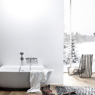 Moderne Badewanne vor einer schlichten weißen Wand, mit Ausblick auf verschneite Landschaft. Holzfußboden, gemütliches Ambiente mit Handtuch und Winterstiefeln. Moderne Badewanne vor einer schlichten weißen Wand, mit Ausblick auf verschneite Landschaft. Holzfußboden, gemütliches Ambiente mit Handtuch und Winterstiefeln.