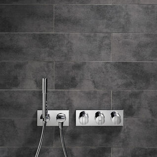 Moderne Dusche mit dunkler Fliesenwand. Ausgestattet mit einem Regenduschkopf und einer Handbrause. Die Armaturen sind in glänzendem Chrom gehalten und haben ein minimalistisches Design. Moderne Dusche mit dunkler Fliesenwand. Ausgestattet mit einem Regenduschkopf und einer Handbrause. Die Armaturen sind in glänzendem Chrom gehalten und haben ein minimalistisches Design.