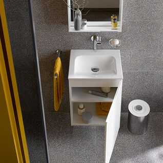 Kleines Bad mit grauen Fliesen. Weißes Waschbecken mit offenem Unterschrank, gelbes Handtuch, Spiegel, graue Vase und silberner Papierkorb. Kleines Bad mit grauen Fliesen. Weißes Waschbecken mit offenem Unterschrank, gelbes Handtuch, Spiegel, graue Vase und silberner Papierkorb.