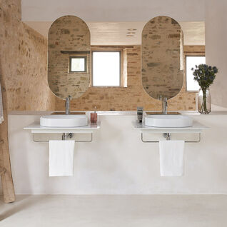 Rustikales Badezimmer mit Natursteinwänden, zwei ovalen Spiegeln, Doppelwaschbecken und dekorativer Holzleiter als Handtuchhalter. Gemütliches Design. Rustikales Badezimmer mit Natursteinwänden, zwei ovalen Spiegeln, Doppelwaschbecken und dekorativer Holzleiter als Handtuchhalter. Gemütliches Design.