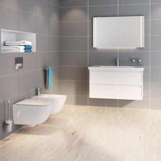 Badezimmer mit grauen Fliesen, wandhängendem WC und Bidet. Weißer Waschtisch mit Spiegel, eingebautes Regal, helle Holzbodenoptik. Badezimmer mit grauen Fliesen, wandhängendem WC und Bidet. Weißer Waschtisch mit Spiegel, eingebautes Regal, helle Holzbodenoptik.