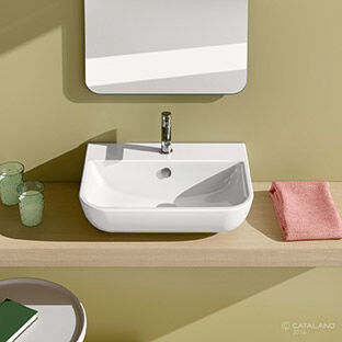 Modernes, abgerundetes Waschbecken auf einer Holzplatte. Daneben ein rosa Handtuch und Glasbecher. Die Wand ist in einem sanften Grünton gehalten, mit einem rechteckigen Spiegel darüber. Modernes, abgerundetes Waschbecken auf einer Holzplatte. Daneben ein rosa Handtuch und Glasbecher. Die Wand ist in einem sanften Grünton gehalten, mit einem rechteckigen Spiegel darüber.