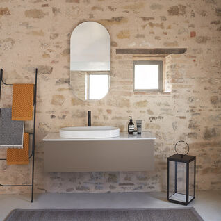 Modernes Badezimmer mit rustikaler Steinwand. Ovaler Spiegel über schlichtem Waschbecken. Dezente Dekoration mit Handtuchleiter und Laterne sorgt für gemütliche Atmosphäre. Modernes Badezimmer mit rustikaler Steinwand. Ovaler Spiegel über schlichtem Waschbecken. Dezente Dekoration mit Handtuchleiter und Laterne sorgt für gemütliche Atmosphäre.