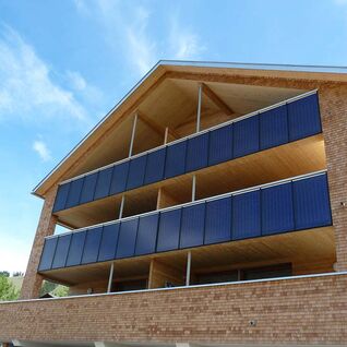 Ein modernes Gebäude mit Solarpaneelen an den Balkonen, gebaut aus Ziegel und Holz, unter einem blauen Himmel. Ein modernes Gebäude mit Solarpaneelen an den Balkonen, gebaut aus Ziegel und Holz, unter einem blauen Himmel.