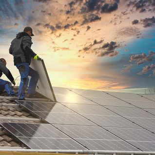 Zwei Arbeiter installieren Solarpaneele auf einem Ziegeldach, während die Sonne am Horizont untergeht und den Himmel in warmen Farben erleuchtet. Zwei Arbeiter installieren Solarpaneele auf einem Ziegeldach, während die Sonne am Horizont untergeht und den Himmel in warmen Farben erleuchtet.