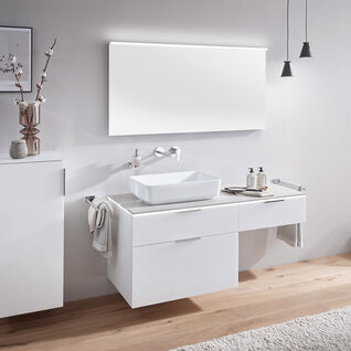 Modernes Badezimmer mit weißem Waschtisch, rechteckigem Spiegel, hohem Schrank, Vase, Pendelleuchten und Holzboden. Minimalistisches Design.