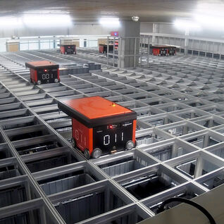 Ein automatisiertes Lagersystem mit mehreren orangefarbenen Robotern, die auf einem Gitterrahmen fahren, um Waren effizient zu bewegen. Ein automatisiertes Lagersystem mit mehreren orangefarbenen Robotern, die auf einem Gitterrahmen fahren, um Waren effizient zu bewegen.