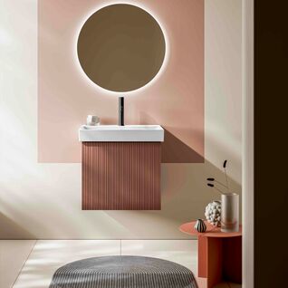 Modernes Bad mit rundem Spiegel, beleuchtet. Minimalistisches Waschbecken, geriffelte Verkleidung, kleiner Tisch mit Deko. Sanfte Farben, stilvoll.