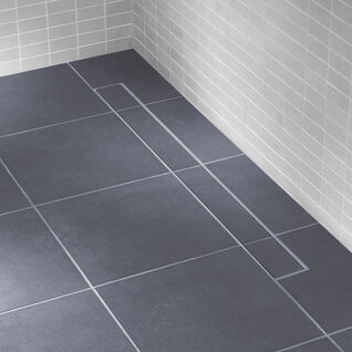 Bodengleiche Dusche mit dunklen Fliesen und einer unauffälligen, in das Fliesenmuster integrierten Ablaufrinne. Helle Wandfliesen betonen das minimalistische Design. Bodengleiche Dusche mit dunklen Fliesen und einer unauffälligen, in das Fliesenmuster integrierten Ablaufrinne. Helle Wandfliesen betonen das minimalistische Design.