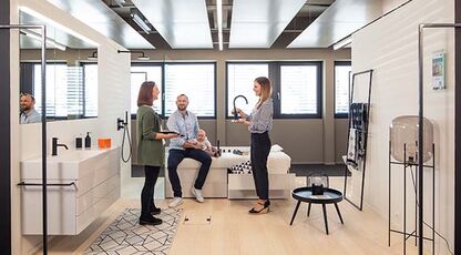 Ein modernes Badezimmer-Showroom mit drei Personen, die sich unterhalten. Der Raum ist hell und minimalistisch, mit stilvoller Einrichtung und Dekor.
