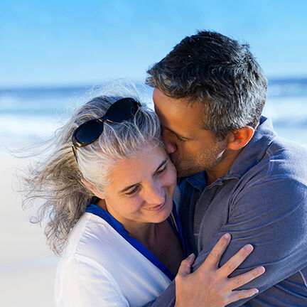 Ein Paar umarmt sich zärtlich am Strand, der Mann küsst die Frau auf die Stirn. Der Himmel ist klar, und die Wellen rollen im Hintergrund. Ein Paar umarmt sich zärtlich am Strand, der Mann küsst die Frau auf die Stirn. Der Himmel ist klar, und die Wellen rollen im Hintergrund.