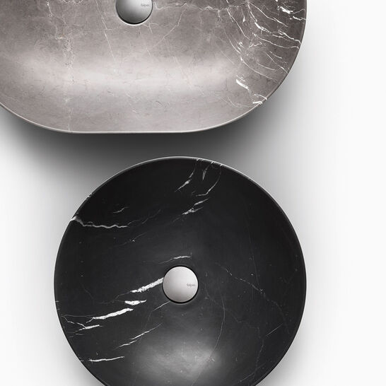 Das Bild zeigt zwei stilvolle Waschbecken aus Marmor. Das obere ist oval und hellgrau, das untere rund und schwarz. Beide haben eine glatte, polierte Oberfl&auml;che mit subtilen Aderungen.