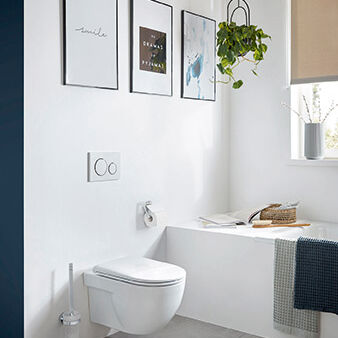 Helles Bad mit wandhängendem WC, grauen Fliesen, dekorativen Bildern, hängender Pflanze und Badewanne neben dem Fenster mit Handtuch und Buch. Helles Bad mit wandhängendem WC, grauen Fliesen, dekorativen Bildern, hängender Pflanze und Badewanne neben dem Fenster mit Handtuch und Buch.