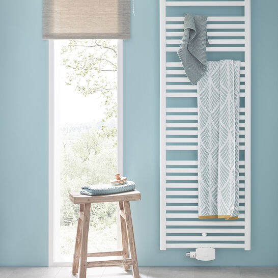 Helles Badezimmer mit blauer Wand, einem weißen Handtuchheizkörper und einem schlichten Holzstuhl. Großes Fenster sorgt für viel natürliches Licht. Helles Badezimmer mit blauer Wand, einem weißen Handtuchheizkörper und einem schlichten Holzstuhl. Großes Fenster sorgt für viel natürliches Licht.