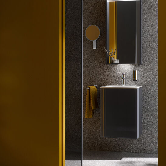 Minimalistisches Badezimmer mit beleuchtetem Spiegel, dunklem Waschtisch, gelben Akzenten und grauem Hintergrund. Minimalistisches Badezimmer mit beleuchtetem Spiegel, dunklem Waschtisch, gelben Akzenten und grauem Hintergrund.
