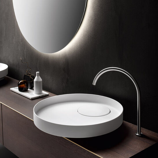 Modernes Badezimmerdesign mit rundem Spiegel und Hinterbeleuchtung, minimalistisches rundes Waschbecken und eleganter, gebogener Armatur. Dunkles Ambiente. Modernes Badezimmerdesign mit rundem Spiegel und Hinterbeleuchtung, minimalistisches rundes Waschbecken und eleganter, gebogener Armatur. Dunkles Ambiente.