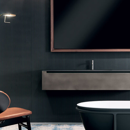 Modernes Badezimmer mit dunklem Stil, minimalistischem Waschtisch, großem Spiegel, elegantem Stuhl und Stehlampe für gemütliches Ambiente.