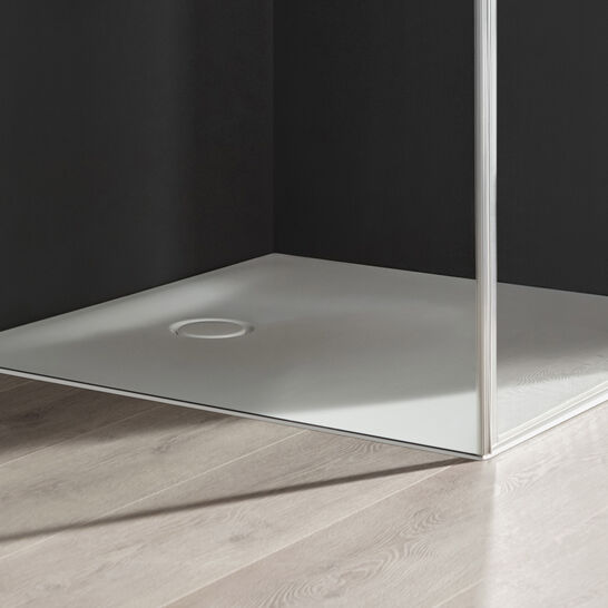 Ecke einer modernen Duschkabine mit klaren Glaswänden und einer weißen Duschwanne. Der Boden besteht aus hellem Holz, daneben ein Korb mit Handtüchern. Ecke einer modernen Duschkabine mit klaren Glaswänden und einer weißen Duschwanne. Der Boden besteht aus hellem Holz, daneben ein Korb mit Handtüchern.