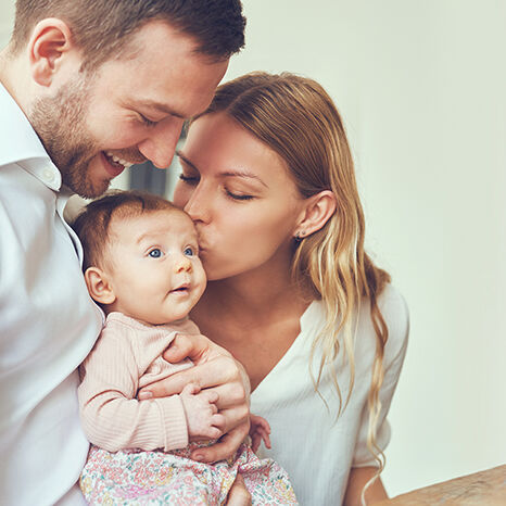 Ein Paar hält liebevoll ein Baby. Die Mutter gibt dem Baby einen Kuss, während der Vater es hält. Es ist eine warme und liebevolle Familienszene. Ein Paar hält liebevoll ein Baby. Die Mutter gibt dem Baby einen Kuss, während der Vater es hält. Es ist eine warme und liebevolle Familienszene.