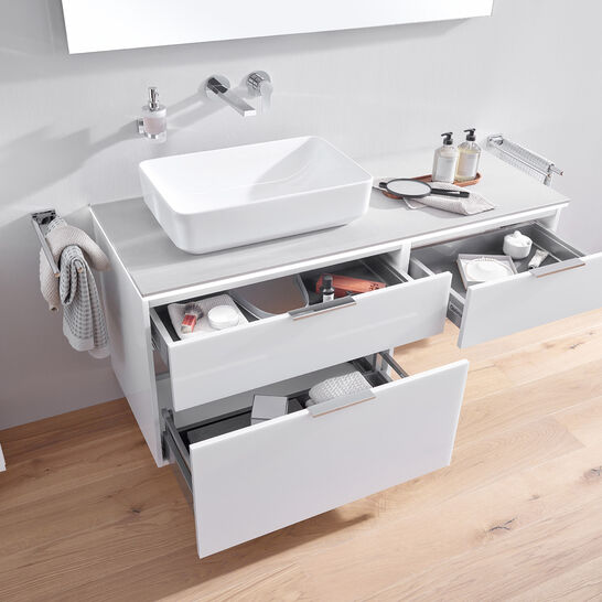 Ein modernes Waschbecken mit offenen Schubladen, gefüllt mit Pflegeprodukten. Auf der Oberfläche stehen Seifenspender und ein kleiner Spiegel, alles in Weiß. Ein modernes Waschbecken mit offenen Schubladen, gefüllt mit Pflegeprodukten. Auf der Oberfläche stehen Seifenspender und ein kleiner Spiegel, alles in Weiß.