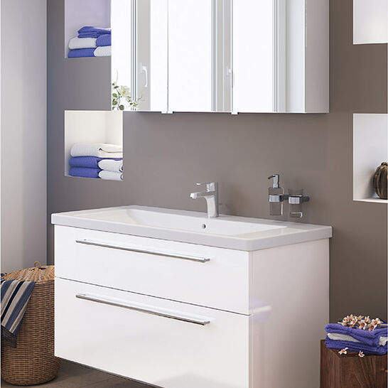 Modernes Badezimmer mit weißem Waschtisch und Spiegel mit Beleuchtung. Eingebaute Regale mit Handtüchern, schlichte Dekoration und neutrale Wandfarben. Modernes Badezimmer mit weißem Waschtisch und Spiegel mit Beleuchtung. Eingebaute Regale mit Handtüchern, schlichte Dekoration und neutrale Wandfarben.