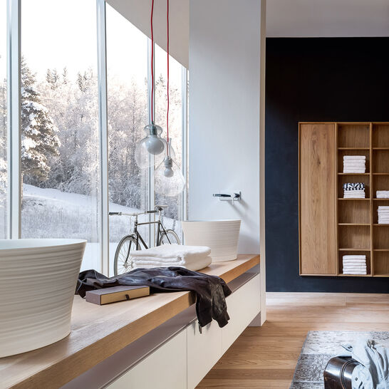 Badezimmer mit großen Fenstern, die ins Freie blicken. Sitzbank mit Holzoberfläche, freistehendes Waschbecken, stilvolle Beleuchtung und Regalwand. Badezimmer mit großen Fenstern, die ins Freie blicken. Sitzbank mit Holzoberfläche, freistehendes Waschbecken, stilvolle Beleuchtung und Regalwand.