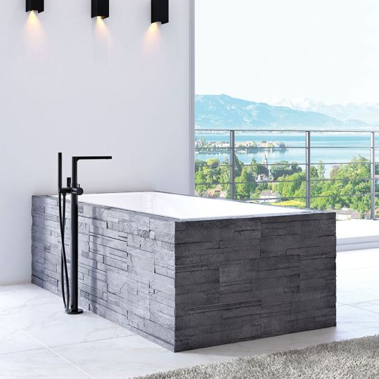 Freistehende Badewanne mit grauer Steinverkleidung, modernem Wasserhahn und Panoramablick. Helle, minimalistische Gestaltung mit Akzentbeleuchtung.