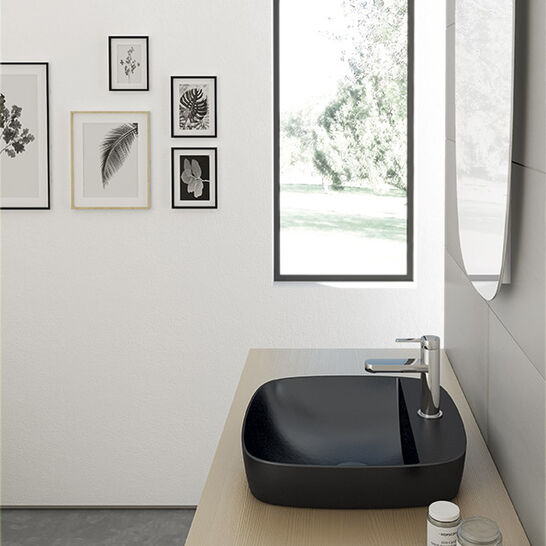 Modernes Bad mit schwarzem quadratischem Waschbecken, Holzoberfläche, dekorativen Bilderrahmen an der Wand und großem Fenster mit Blick ins Freie. Modernes Bad mit schwarzem quadratischem Waschbecken, Holzoberfläche, dekorativen Bilderrahmen an der Wand und großem Fenster mit Blick ins Freie.