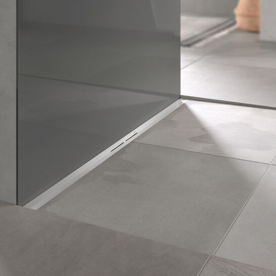 Moderne Dusche mit Glaswand, grauen Fliesen und ebenerdiger Entwässerung. Minimalistisches Design mit einem Teil einer Toilette im Hintergrund. Moderne Dusche mit Glaswand, grauen Fliesen und ebenerdiger Entwässerung. Minimalistisches Design mit einem Teil einer Toilette im Hintergrund.