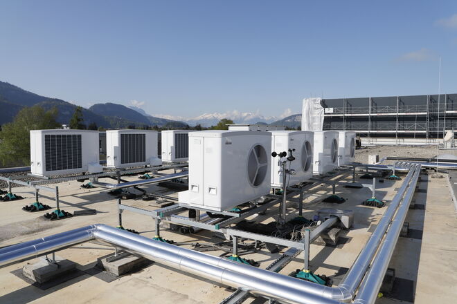 Auf einem Flachdach sind mehrere große Klimaanlagen oder Lüftungseinheiten installiert. Im Hintergrund sind Berge zu sehen. Die Anlage ist mit verschiedenen Rohrleitungen verbunden. Auf einem Flachdach sind mehrere große Klimaanlagen oder Lüftungseinheiten installiert. Im Hintergrund sind Berge zu sehen. Die Anlage ist mit verschiedenen Rohrleitungen verbunden.