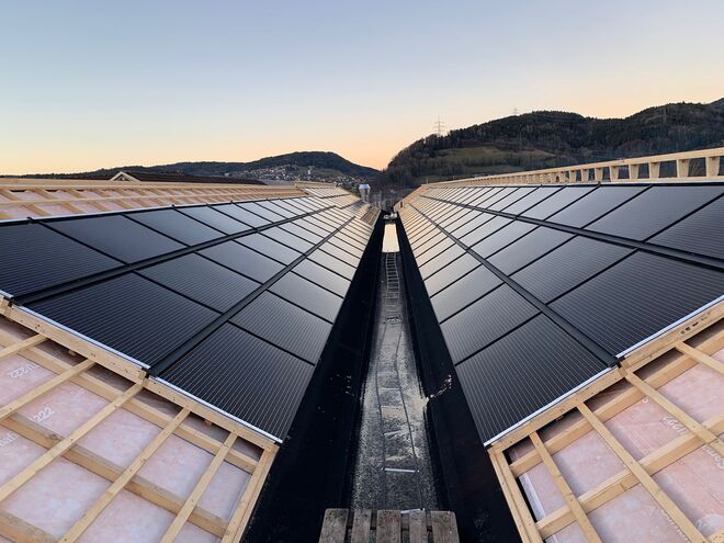 Solarpaneele auf einem V-förmigen Dach, eingebettet in eine hügelige Landschaft bei Sonnenuntergang. Solarpaneele auf einem V-förmigen Dach, eingebettet in eine hügelige Landschaft bei Sonnenuntergang.