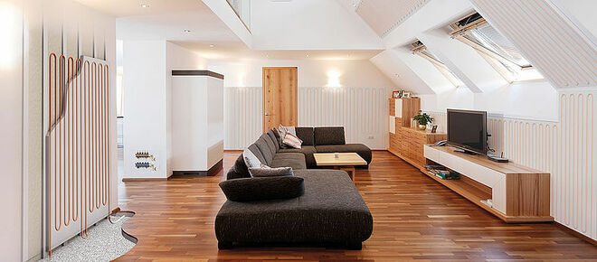 Modernes Wohnzimmer mit Dachschrägen, einer großen schwarzen Couch, Holzböden und einem Flachbildfernseher auf einem Holzregal. Modernes Wohnzimmer mit Dachschrägen, einer großen schwarzen Couch, Holzböden und einem Flachbildfernseher auf einem Holzregal.