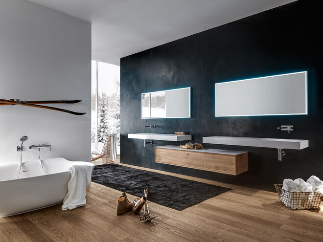 Badezimmer mit freistehender Badewanne, beleuchteten Spiegeln, Holzwaschtisch, Skiern an der Wand und großem Fenster. Elegante, gemütliche Atmosphäre. Badezimmer mit freistehender Badewanne, beleuchteten Spiegeln, Holzwaschtisch, Skiern an der Wand und großem Fenster. Elegante, gemütliche Atmosphäre.