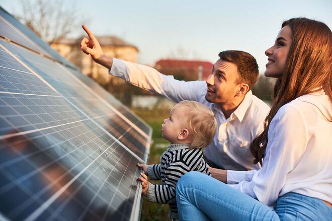 Eine Familie betrachtet Solarpaneele im Freien. Ein Erwachsener zeigt auf etwas, während ein Kind die Paneele berührt. Eine Familie betrachtet Solarpaneele im Freien. Ein Erwachsener zeigt auf etwas, während ein Kind die Paneele berührt.