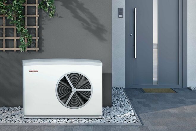 Das Bild zeigt eine Außeneinheit einer Wärmepumpe von Stiebel Eltron neben einer Haustür, umgeben von Kieselsteinen und Kletterpflanzen an der Wand. Das Bild zeigt eine Außeneinheit einer Wärmepumpe von Stiebel Eltron neben einer Haustür, umgeben von Kieselsteinen und Kletterpflanzen an der Wand.