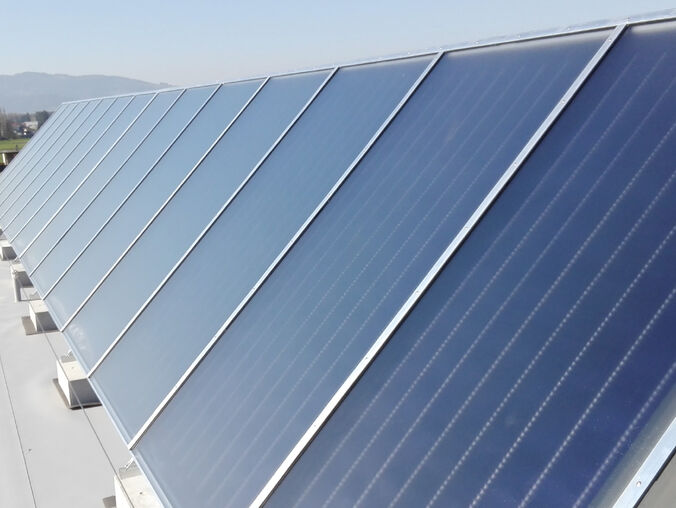Eine Reihe von Solarpanelen auf einem Dach, ausgerichtet zur optimalen Energiegewinnung, mit einer Landschaft und Bergen im Hintergrund.
