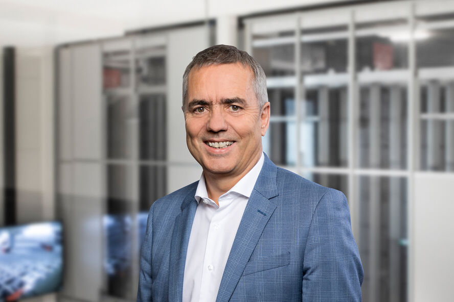 Ein lächelnder Mann in einem blauen Anzug steht vor einem modernen Bürohintergrund mit Glaswänden und technologiebezogener Einrichtung. Ein lächelnder Mann in einem blauen Anzug steht vor einem modernen Bürohintergrund mit Glaswänden und technologiebezogener Einrichtung.